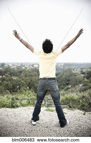 Stock Image - African American man with arms outstretched in remote area. Fotosearch