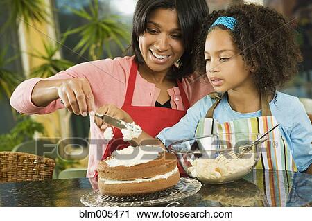 Stock Image - African American mother and daughter frosting cake. Fotosearch