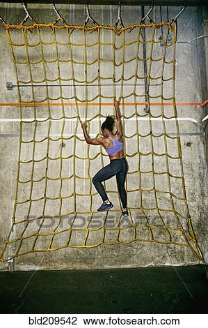 Stock Image - African American woman climbing net wall in gym. Fotosearch