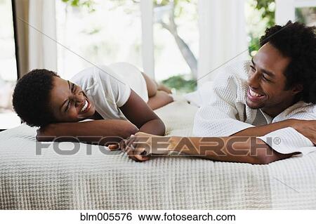Stock Photograph - African American woman laying with boyfriend on bed. Fotosearch
