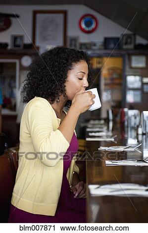 Stock Image - African American woman sipping coffee at diner counter. Fotosearch