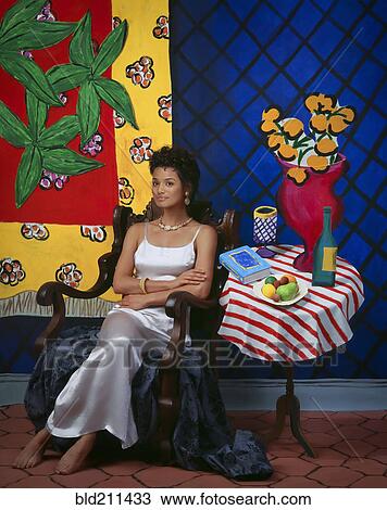 Stock Image - African American woman sitting at still life wall art. Fotosearch