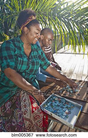 Stock Photo - African American woman solving puzzle with family on patio. Fotosearch