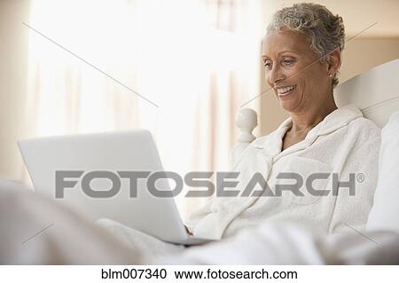 Stock Image - African American woman using laptop in bed. Fotosearch