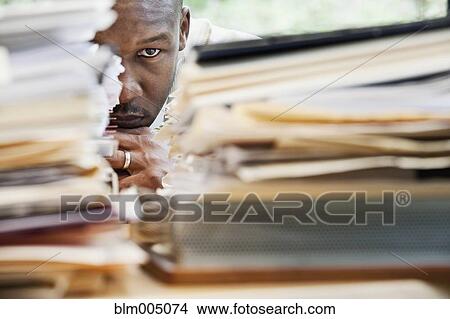 Picture - African businessman hiding behind stack of paperwork. Fotosearch