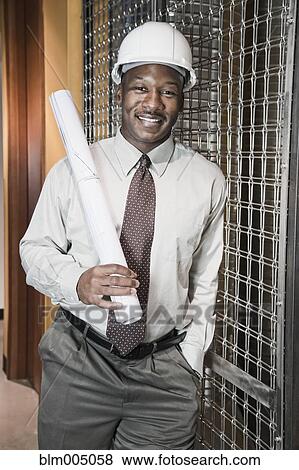 Stock Photo - African businessman in hard-hat holding blueprints. Fotosearch
