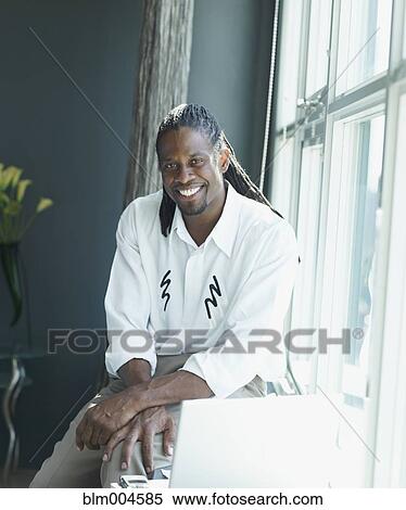Stock Photography - African businessman sitting on windowsill. Fotosearch