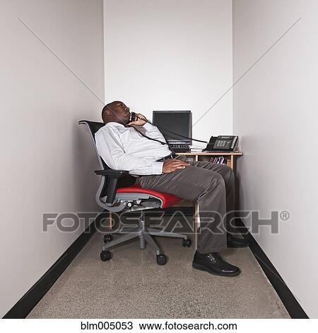 Stock Image - African businessman talking on phone in small office. Fotosearch