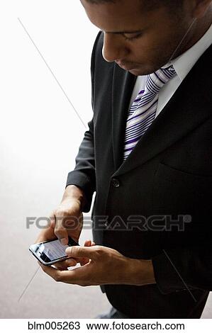 Stock Image - African businessman text messaging on cell phone. Fotosearch