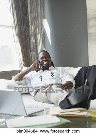 Picture - African businessman with feet up talking on cell phone. Fotosearch