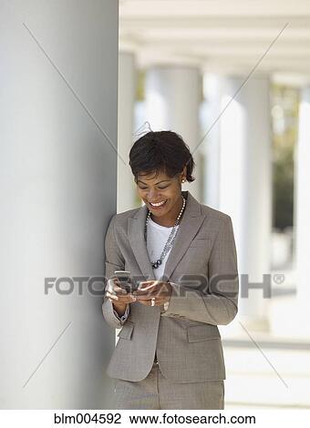 Stock Image - African businesswoman text messaging on cell phone. Fotosearch