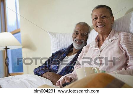 Stock Image - African couple drinking coffee in bed. Fotosearch