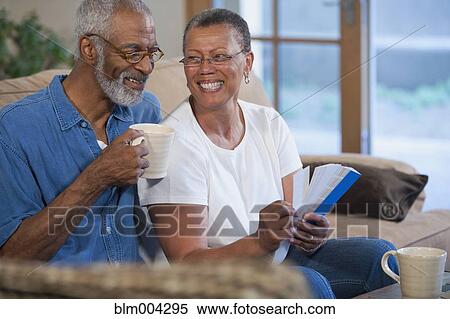 Stock Photography - African couple looking at paint swatches on sofa. Fotosearch