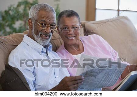 Stock Image - African couple reading newspaper on sofa. Fotosearch
