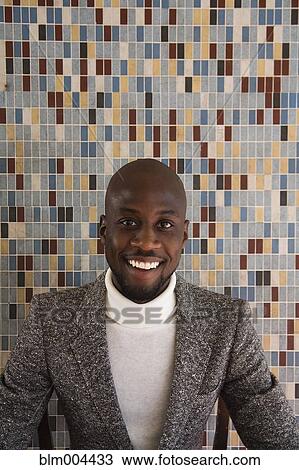 Stock Image - African man in tweed jacket smiling in front of tiled wall. Fotosearch