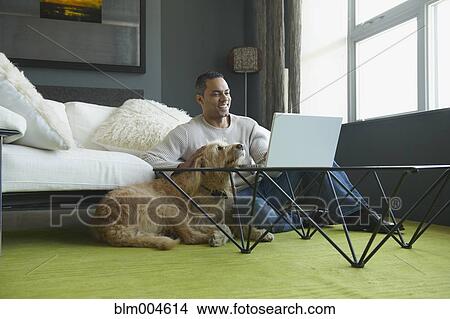 Picture - African man using laptop as dog sits nearby. Fotosearch