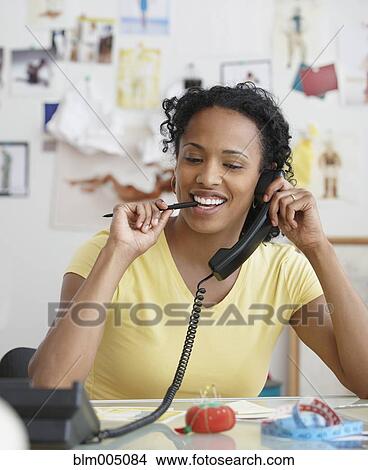 Picture - African seamstress talking on telephone. Fotosearch