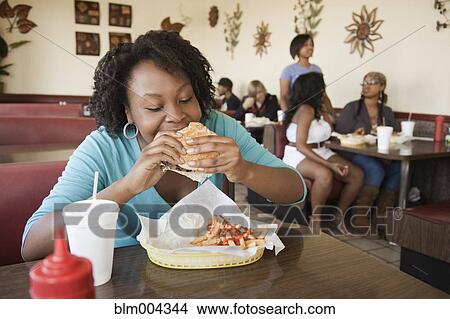 African woman eating hamburger in diner View Large Photo Image Picture - African woman eating hamburger in diner. Fotosearch