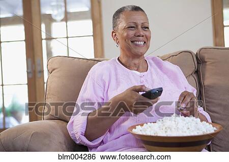 African woman holding remote control and eating popcorn on sofa View Large Photo Image Stock Photograph - African woman holding remote control and eating popcorn on sofa. Fotosearch