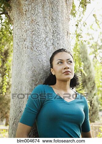 Picture - African woman leaning against tree. Fotosearch