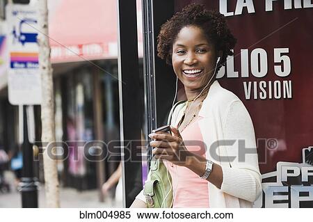 Stock Photography - African woman listening to mp3 player at bus stop. Fotosearch