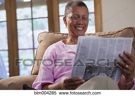 Stock Photography - African woman reading newspaper on sofa. Fotosearch