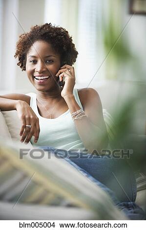 Picture - African woman talking on cell phone in living room. Fotosearch