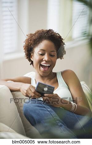 African woman text messaging on cell phone in living room View Large Photo Image Stock Photography - African woman text messaging on cell phone in living room. Fotosearch