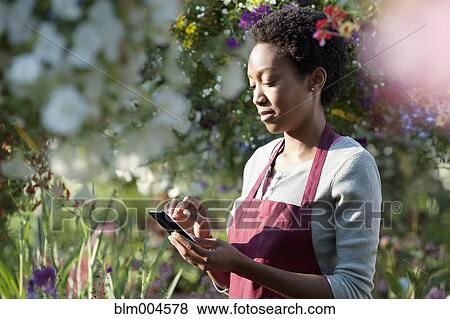 Stock Photo - African woman working in garden nursery checking cell phone. Fotosearch