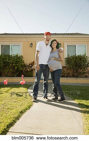 Stock Photograph - Alternative Hispanic couple standing in front of house. Fotosearch