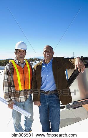 Stock Image - Architect and construction worker on rooftop. Fotosearch