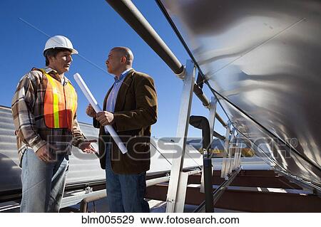 Stock Photo - Architect and construction worker on rooftop near solar panels. Fotosearch