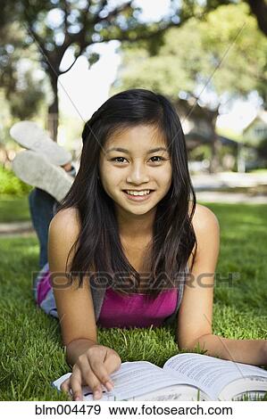 Stock Photo - Asian girl laying in grass reading book. Fotosearch