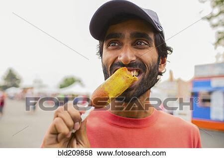 Asian man eating corn dog outdoors View Large Photo Image Stock Photo - Asian man eating corn dog outdoors. Fotosearch