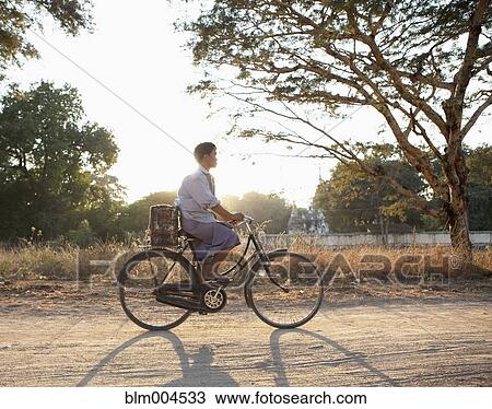 Stock Image - Asian man riding bicycle on dirt road. Fotosearch