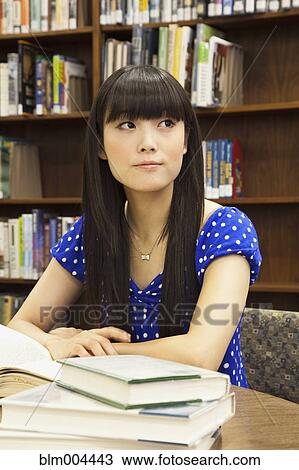 Stock Image - Asian woman doing homework in library. Fotosearch