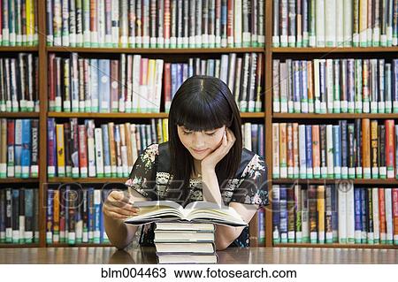 Stock Image - Asian woman reading book in library. Fotosearch