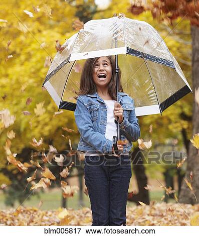 Stock Photo - Autumn leaves falling on mixed race girl with umbrella. Fotosearch