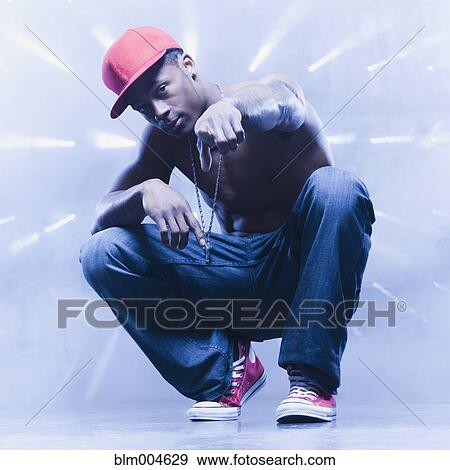 Stock Photo - Back lit African man squatting and pointing. Fotosearch