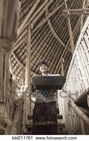 Stock Image - Balinese man carrying basket in hotel, Ubud, Bali, Indonesia. Fotosearch