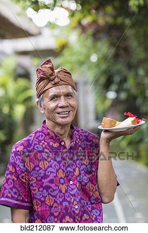 Balinese server carrying plate of food View Large Photo Image Stock Photo - Balinese server carrying plate of food. Fotosearch