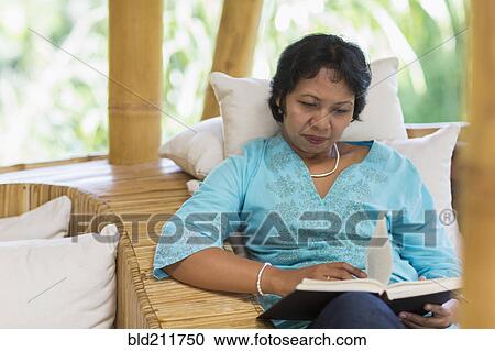 Stock Image - Balinese woman reading in armchair. Fotosearch