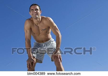 Stock Photo - Bare chested Hispanic man leaning on knees. Fotosearch