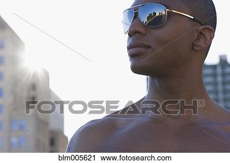 Stock Image - Bare chested mixed race man wearing sunglasses. Fotosearch