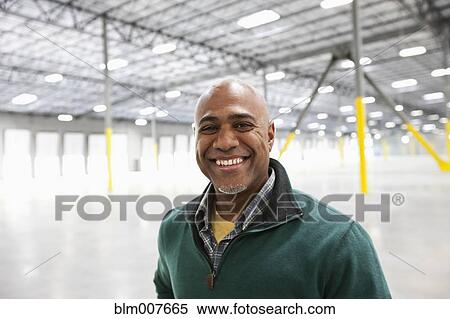 Stock Photography - Black businessman standing in empty warehouse. Fotosearch