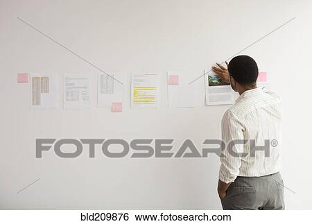 Stock Photograph - Black businessman taping up papers on office wall. Fotosearch