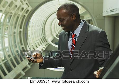 Stock Image - Black businessman text messaging on cell phone. Fotosearch