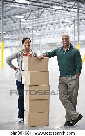 Stock Image - Black co-workers standing with boxes in empty warehouse. Fotosearch