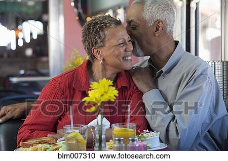 Stock Image - Black couple whispering in restaurant. Fotosearch