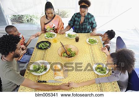 Stock Image - Black family saying grace at dining room table. Fotosearch